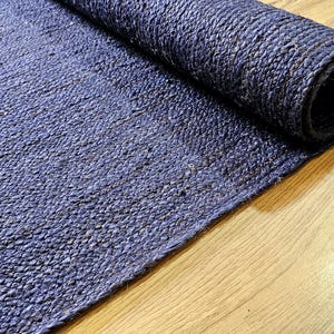 Op de afbeelding: Een close-up van een blauw jute tapijt dat opgerold is op een houten vloer. Het tapijt is gemaakt van natuurlijke vezels en heeft een textuur.