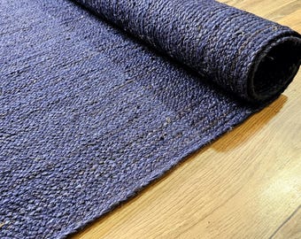 Könnte beinhalten: Nahaufnahme eines blauen Juterugs, der auf einem Holzboden aufgerollt ist. Der Teppich besteht aus Naturfasern und hat eine strukturierte Oberfläche.