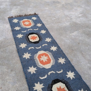 May include: A blue and orange patterned rug with a geometric design. The rug has a fringe on the top edge.