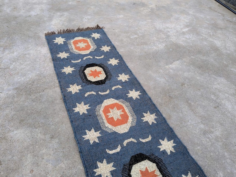 May include: A blue and orange patterned rug with a geometric design. The rug has a fringe on the top edge.