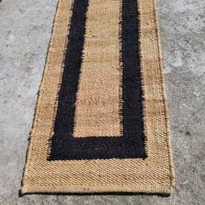 May include: A natural fiber rug with a black border. The rug has a woven texture and is rectangular in shape.