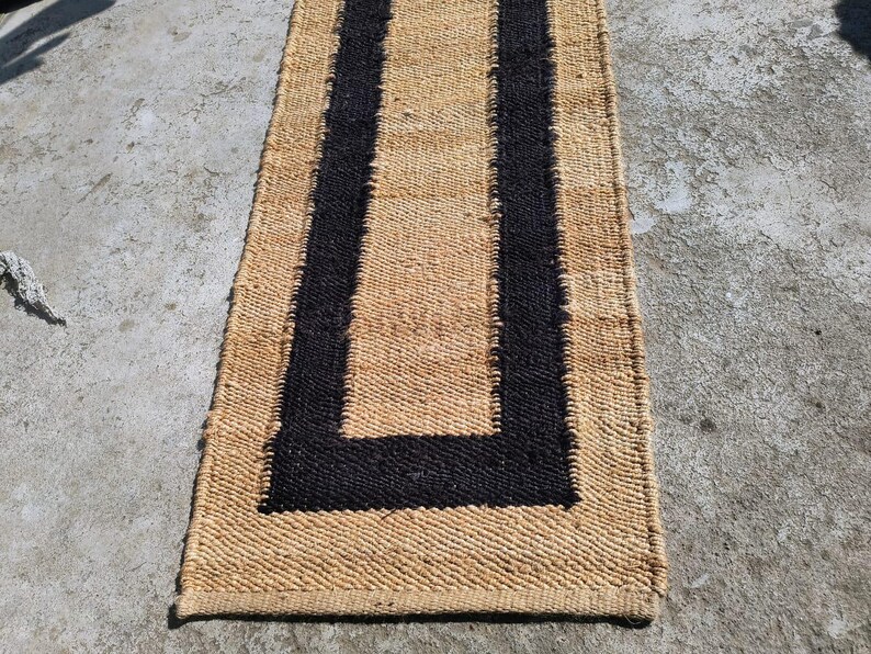 May include: A natural fiber rug with a black border. The rug has a woven texture and is rectangular in shape.