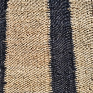 May include: A woven rug with black and natural brown stripes. The rug is made of natural fibers and has a textured surface.