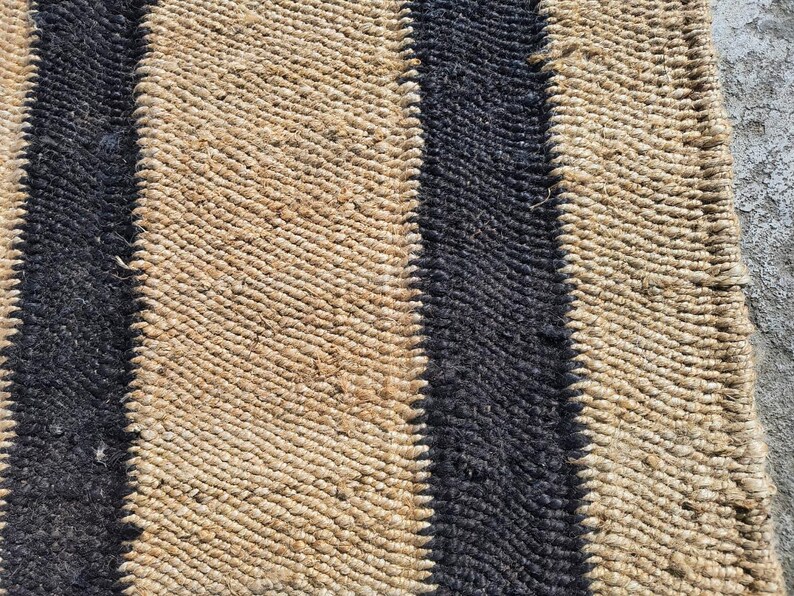 May include: A woven rug with black and natural brown stripes. The rug is made of natural fibers and has a textured surface.