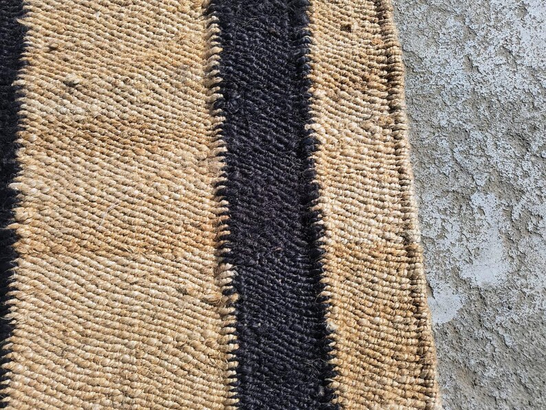 May include: A natural fiber rug with a black stripe down the center. The rug is woven with a textured pattern.