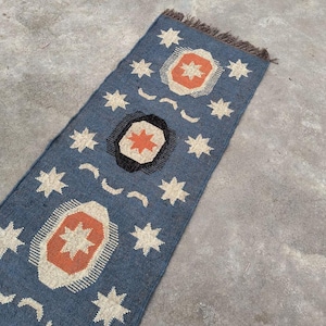 May include: A blue and orange patterned rug with a fringed border. The rug features a repeating design of stars and geometric shapes.