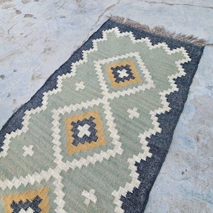 May include: A green, black, and yellow patterned rug with a geometric design. The rug has a fringe border.