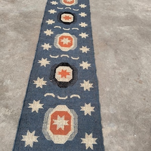 May include: A blue and white runner rug with a geometric pattern of stars and circles. The circles have a red and orange center.