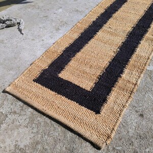 May include: A natural fiber rug with a black border. The rug has a rectangular shape and is made of woven material.