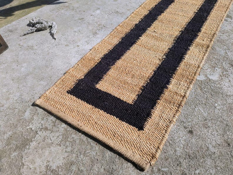 May include: A natural fiber rug with a black border. The rug has a rectangular shape and is made of woven material.