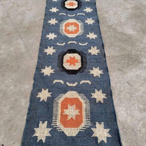 May include: A blue and white patterned rug with a geometric design. The rug has a fringe border and is made of woven fabric.