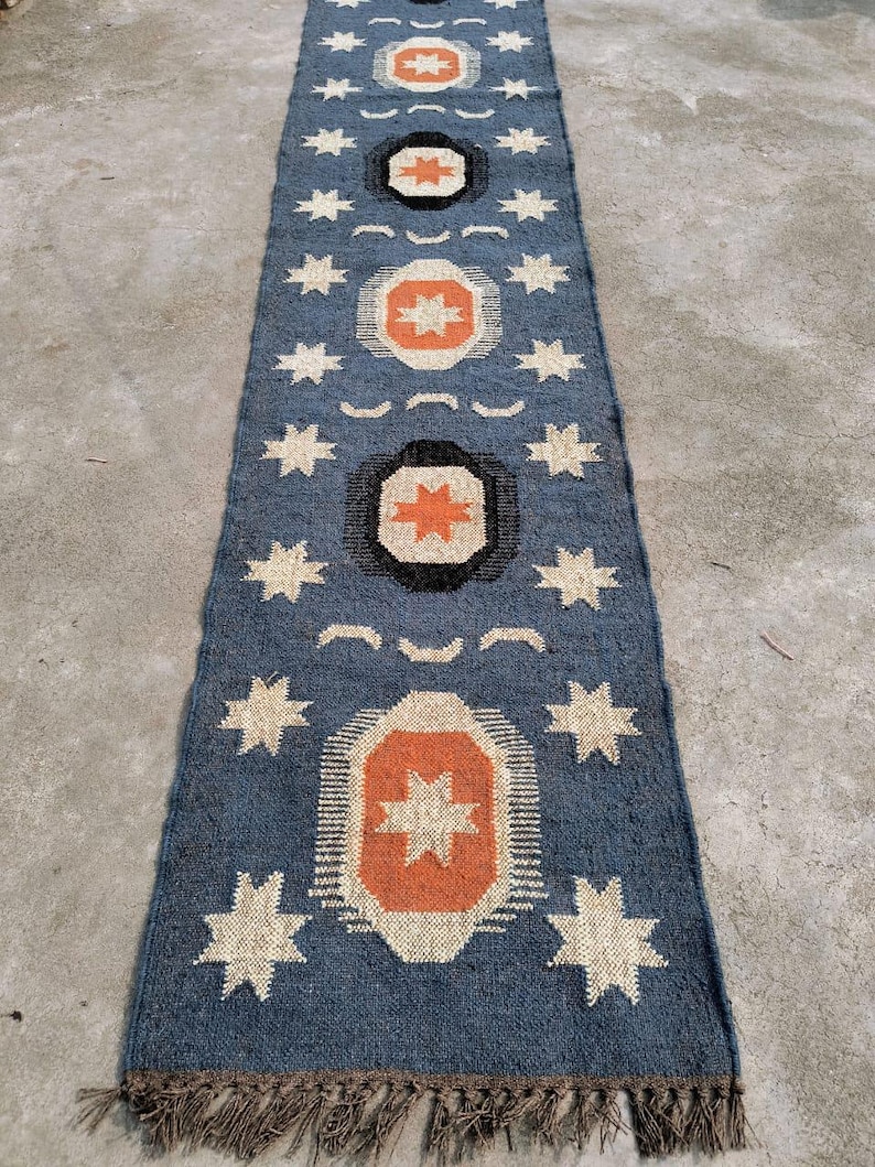 May include: A blue and white patterned rug with a geometric design. The rug has a fringe border and is made of woven fabric.