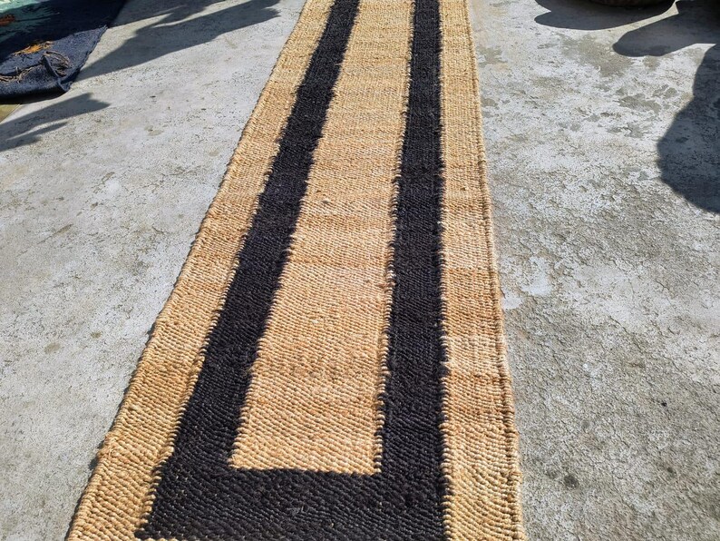 May include: A natural fiber rug with a black and tan striped pattern. The rug is woven with a thick, textured material and has a long, rectangular shape.