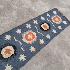 May include: A blue and white patterned rug with orange accents. The rug features a repeating design of stars and circles.
