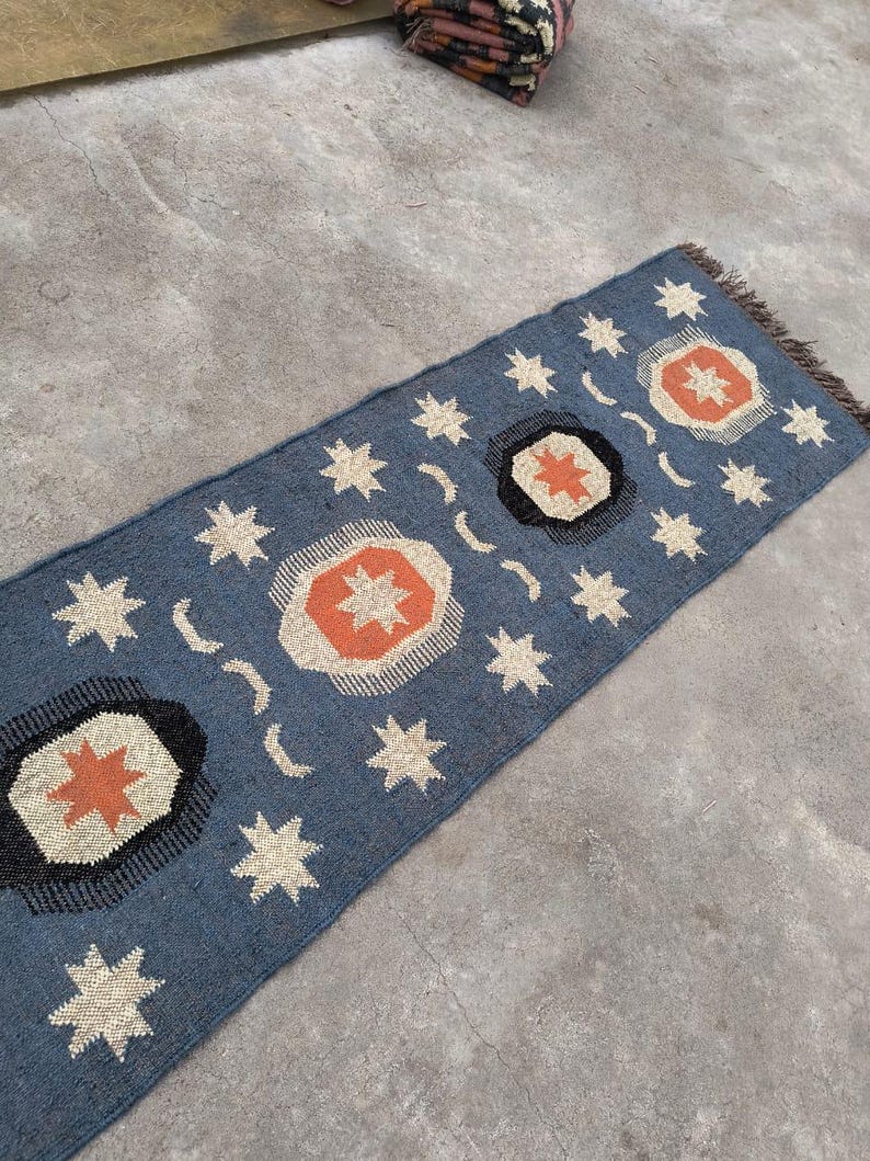 May include: A blue and white patterned rug with orange accents. The rug features a repeating design of stars and circles.