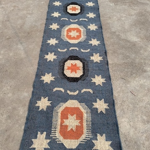 May include: A blue and orange patterned rug with a geometric design. The rug has a fringe border and features a repeating pattern of stars and circles.