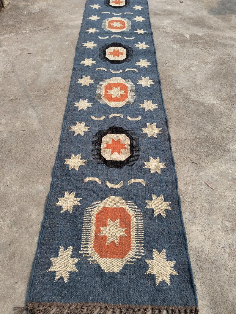 May include: A blue and orange patterned rug with a geometric design. The rug has a fringe border and features a repeating pattern of stars and circles.