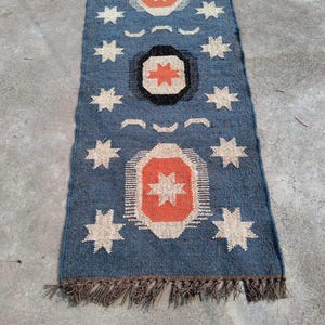 May include: A blue and orange patterned rug with a fringe border. The rug has a geometric design with stars and circles.