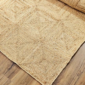 Op de afbeelding: Een vloerkleed van natuurlijke vezels met een geweven patroon in een lichtbruine kleur. Het vloerkleed is gemaakt van jute en heeft een natuurlijke, aardse uitstraling.