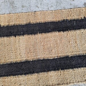 May include: A natural fiber rug with a striped pattern. The rug has alternating bands of natural tan and black.