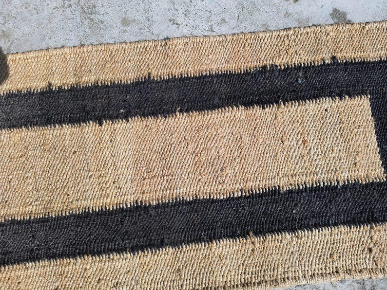 May include: A natural fiber rug with a striped pattern. The rug has alternating bands of natural tan and black.