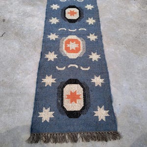 May include: A blue and orange patterned rug with a fringe border. The rug has a geometric design with stars and circles.
