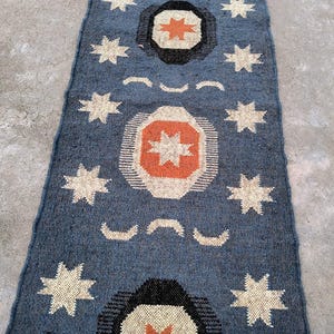 May include: A blue and white patterned rug with a geometric design featuring stars and circles. The rug has a distressed look and is made of natural fibers.