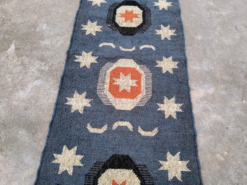 May include: A blue and white patterned rug with a geometric design featuring stars and circles. The rug has a distressed look and is made of natural fibers.