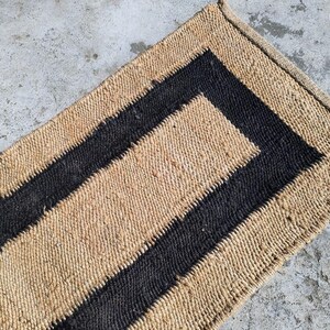May include: A natural fiber rug with a black border. The rug has a woven texture and is made of natural materials.