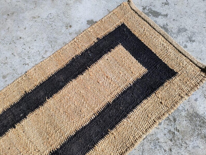 May include: A natural fiber rug with a black border. The rug has a woven texture and is made of natural materials.