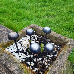 May include: A stone planter filled with white gravel and small black mushrooms. The mushrooms are made of metal and have a shiny, silver finish.
