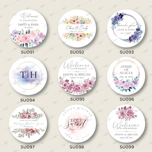 Op de afbeelding: Negen ronde stickers voor bruiloften of bruidsdouches met bloemmotieven. De stickers bevatten verschillende teksten, waaronder "Welkom op onze bruiloft", "Bedankt", "Liefde is zoet" en "Ashleys bruidsdouche".