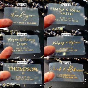 Peut inclure: Dix boîtes de faveur en plastique transparent avec des lettres dorées. Les boîtes présentent différents noms et adresses. Le texte comprend "merci", "Emma & John Smith", "Megan & Harvey Cooper", "Kelsey Dylan", "Thompson", et "Jacob & Rebecca".