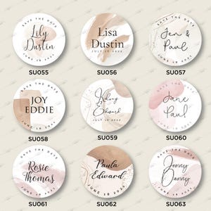 Op de afbeelding: Negen ronde save-the-date kaarten met aquarel achtergronden in roze en bruine tinten. Elke kaart heeft de namen van een stel en de trouwdatum. De kaarten zijn gelabeld met de productcode SU055 tot en met SU063.
