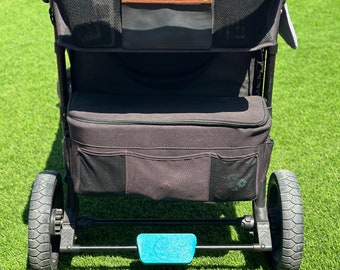 May include: A black stroller with a brown leather handle and a black storage bag with the word "Wonderfold" on it. The stroller has a blue footrest and black wheels.