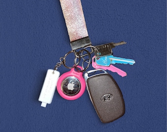 May include: A set of keys with a pink and white keychain, a pink key fob with an apple logo, a brown car key fob with a Hyundai logo, and a white key fob with the text "Smart Key" on it.