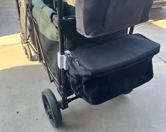 May include: A black wagon with a green fabric seat and a black handle. The wagon has a black cooler bag attached to the back and a black mesh bag with a brown leather patch attached to the handle.