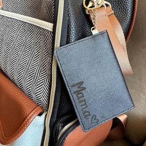 May include: A black leather keychain with a silver key ring and a brown strap. The keychain has the word "Mama" engraved on it with a small heart.
