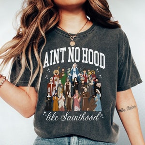 May include: A dark gray t-shirt with a white graphic print of a group of saints and the text "Ain't no hood like Sainthood".