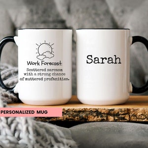 May include: White ceramic mug with a black handle and rim. The mug features a black and white illustration of a sun and clouds with the text "Work Forecast: Scattered sarcasm with a strong chance of muttered profanities." The second mug is white with a black handle and rim and the name "Sarah" printed in black.