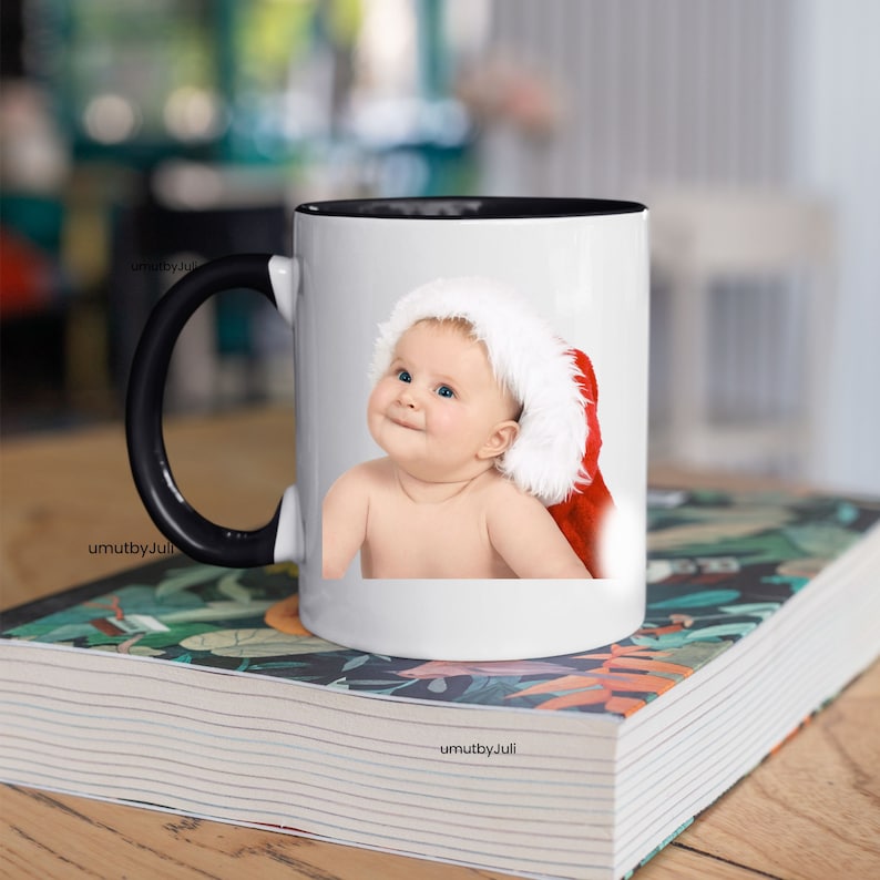 May include: White ceramic mug with a black handle. The mug features a printed image of a baby wearing a Santa hat.