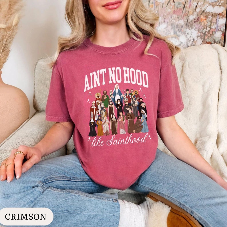 May include: A crimson t-shirt with a white graphic print that says "Ain't no hood like Sainthood." The graphic features a group of cartoon saints.