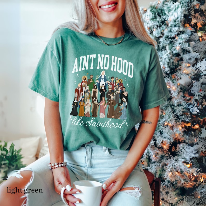 May include: A light green t-shirt with the text "Ain't no hood like Sainthood" and a graphic of a group of saints.