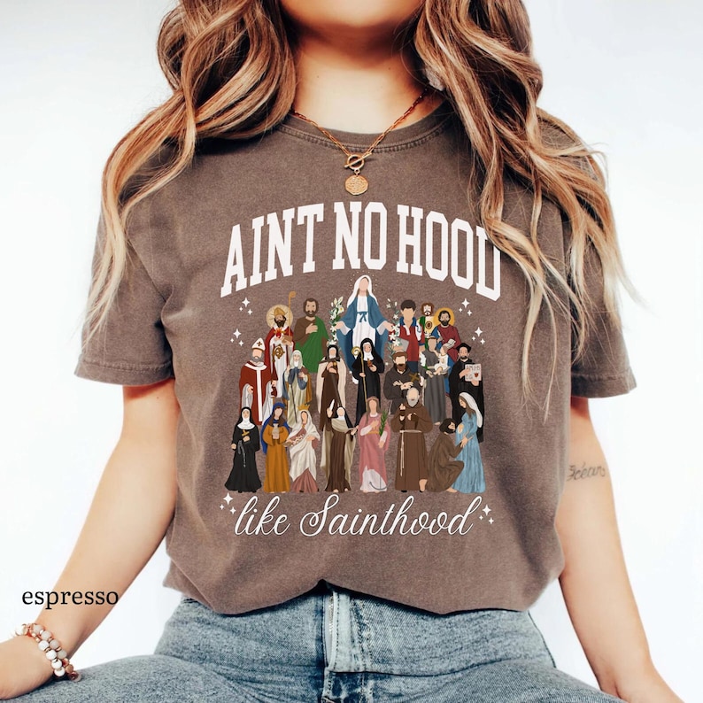 May include: A brown t-shirt with the text "Ain't no hood like Sainthood" and an illustration of a group of saints.