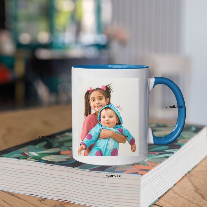 May include: White ceramic mug with a blue rim and handle. The mug features a photo of two children, a girl with brown hair and a boy with a blue and purple monster costume. The photo is on a white background.