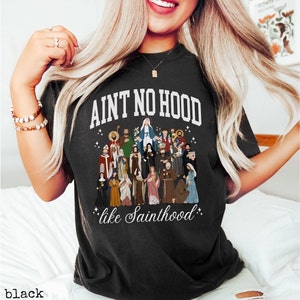 May include: Black t-shirt with a white graphic that says "Ain't No Hood Like Sainthood" and features a colorful illustration of a group of saints.
