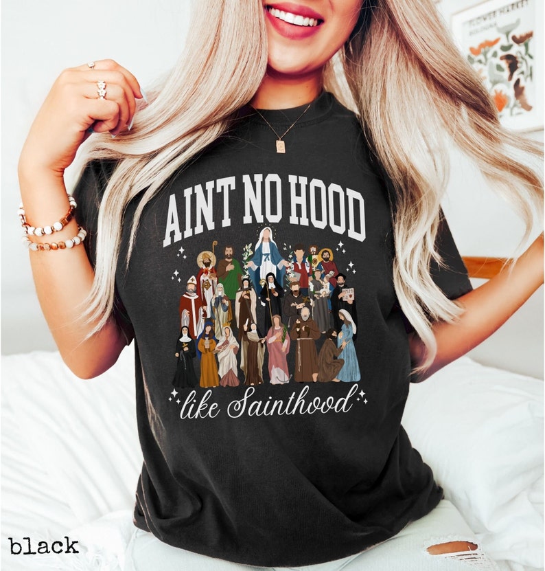May include: Black t-shirt with a white graphic that says "Ain't No Hood Like Sainthood" and features a colorful illustration of a group of saints.