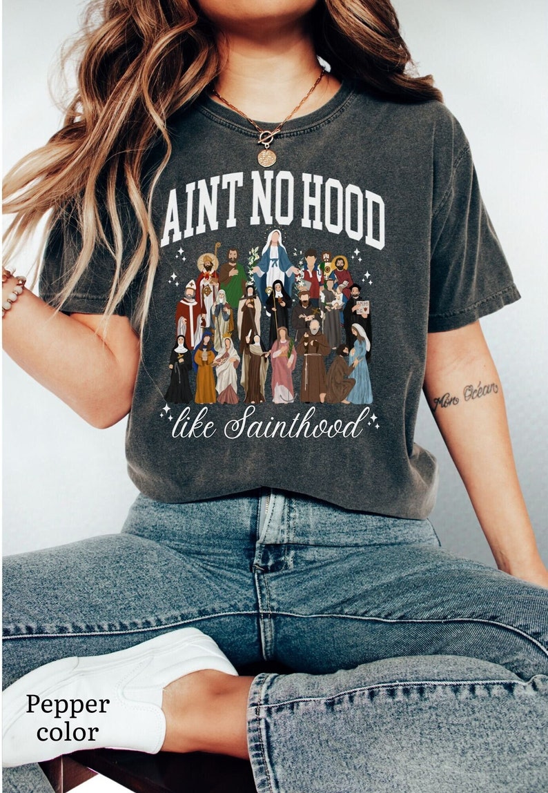 May include: A dark gray t-shirt with a white graphic print of a group of saints and the text "Ain't no hood like Sainthood".