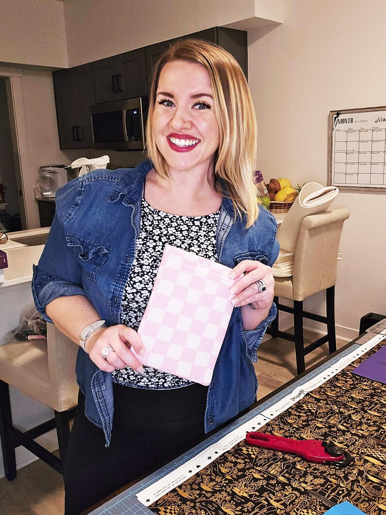 Puede incluir: Una mujer sostiene una bolsa de tela a cuadros rosa y blanca. La bolsa est&aacute; hecha de una tela suave y acolchada. La mujer lleva una chaqueta vaquera azul y una camisa de flores blancas y negras. Est&aacute; de pie en una habitaci&oacute;n con una mesa y una silla.