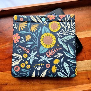 May include: A dark blue e-reader case with a floral pattern featuring sunflowers, leaves, and small flowers in shades of yellow, pink, and green.